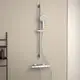 Brausethermostat in Chrom mit handgehaltener Dusche und Ablage, montiert an einer hellen Wand. Ein Produkt der Marke Ideal Standard.